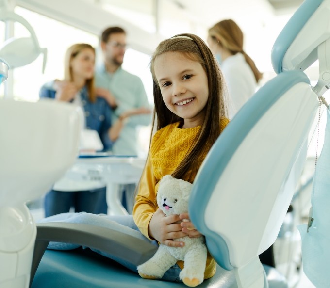 Smiling girl in dental chair holding a teddy bear