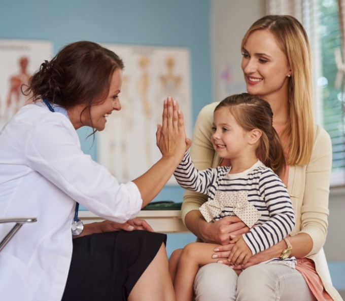 Pediatrician giving high five to young girl sitting on her mothers lap