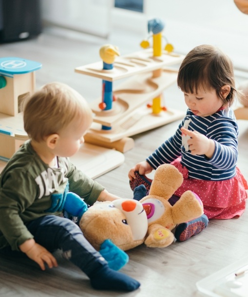 Two babies sitting on floor playing with toys